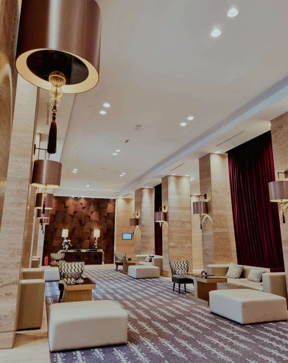 Lounge de lobby com iluminação quente, poltronas e cortinas em tom bordô
